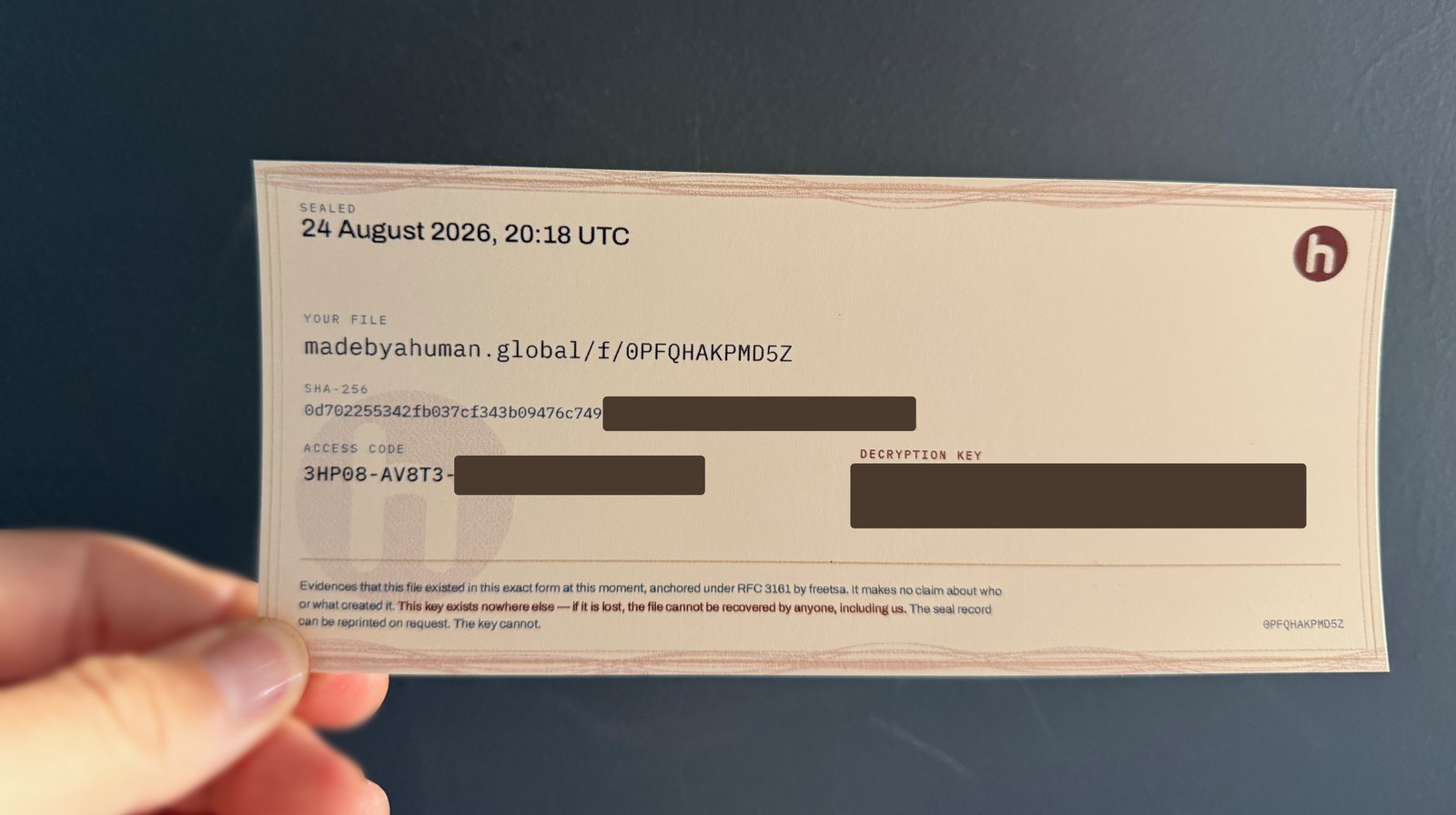 A printed certificate held in one hand: the file's address, its SHA-256 fingerprint and the moment it was sealed, with the decryption key covered.